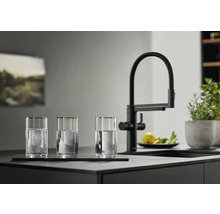 Trois verres d'eau à côté d'un robinet de cuisine noir sur un comptoir de cuisine.