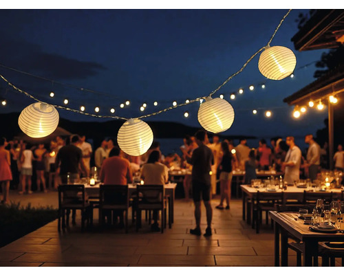 Beleuchtete Papierlaternen-Lichterkette über Tischen im Freien bei einer abendlichen Veranstaltung