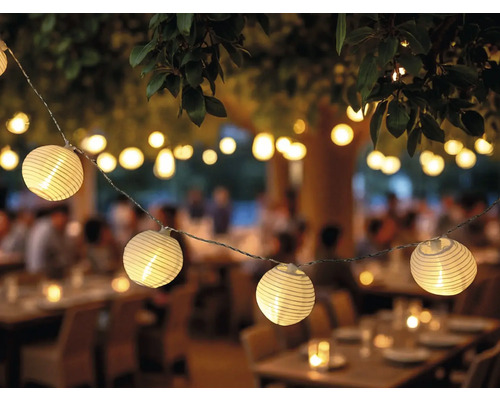 Dekorative Lichterkette mit runden Lampen im Aussenbereich über Tischen