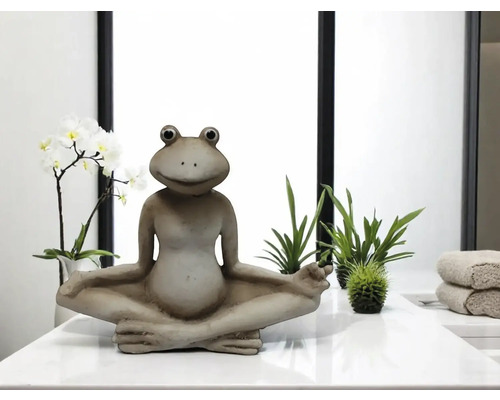 Décoration d'une figurine de grenouille assise avec des plantes sur une surface blanche