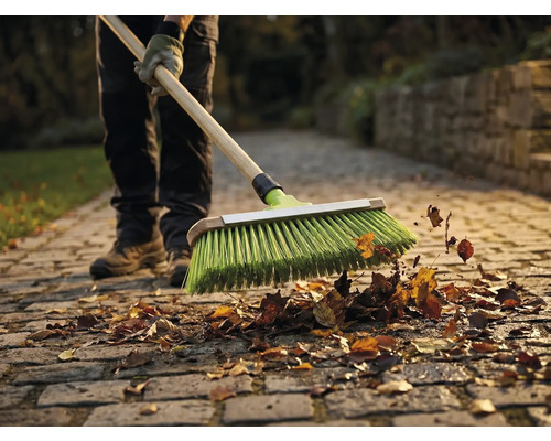 Eine Person kehrt Laub mit einem Besen auf einem Steinpflasterweg.