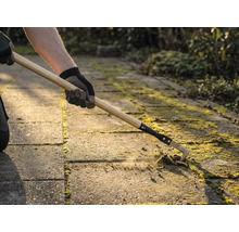 Eine Person entfernt mit einem Fugenreiniger Moos zwischen Pflastersteinen.