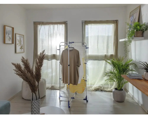 Espace de vie avec séchoir à linge, vêtements, fenêtres avec rideaux et décorations.