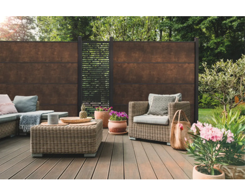 Terrasse moderne avec clôture brise-vue aspect rouille, meubles de jardin en résine tressée et lames de terrasse dans un jardin.