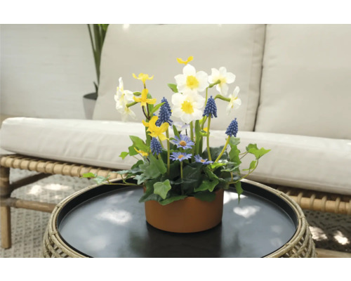 Blumenarrangement mit Narzissen, Traubenhyazinthen und Gänseblümchen in einem braunen Topf auf einem Tisch