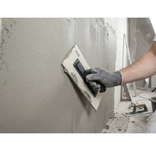 Artisan lissant un mur avec une taloche et du mastic.