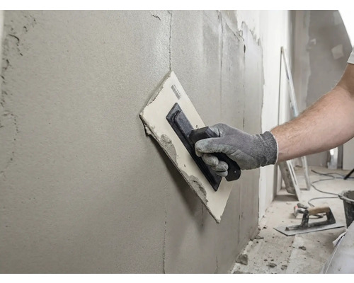 Artisan lissant un mur avec une taloche et du mastic.