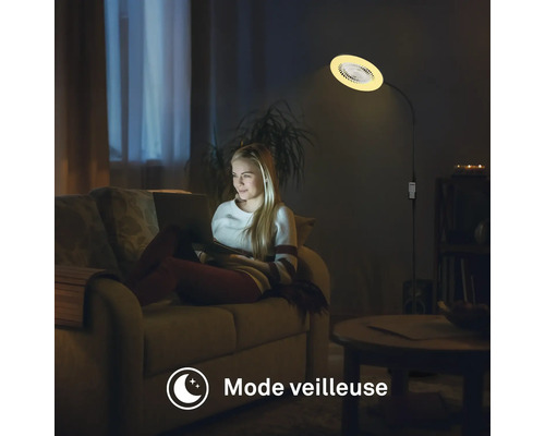 Une femme assise sur un canapé avec un ordinateur portable, tandis qu'un lampadaire illumine la pièce