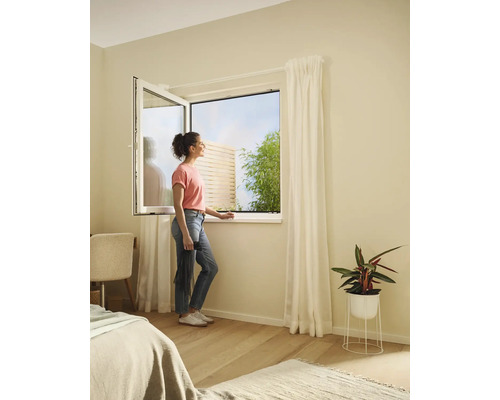 Frau am offenen Fenster mit Insektenschutzgitter im Schlafzimmer