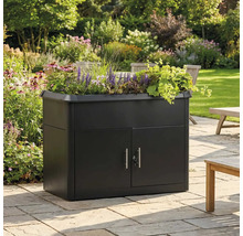 Armoire de jardin noire avec jardinière intégrée, garnie de fleurs sur une terrasse en pierre dans un jardin lumineux.