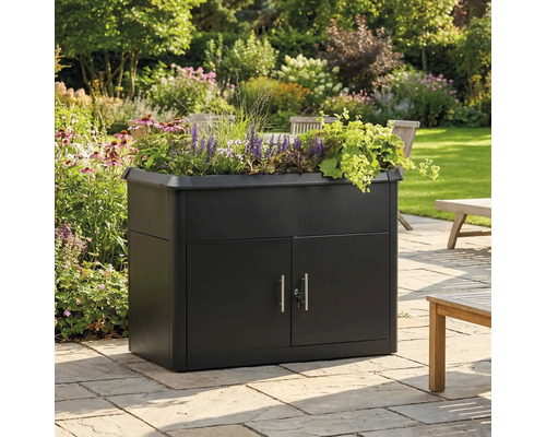 Armoire de jardin noire avec jardinière intégrée, garnie de fleurs sur une terrasse en pierre dans un jardin lumineux.