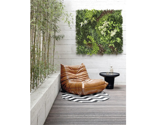 Scène avec un fauteuil, une table, un tapis rond et un panneau mural vert sur une terrasse