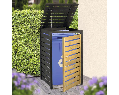 Cache-poubelle en bois avec cadre noir et porte en bois naturel, abritant une poubelle bleue sur une terrasse en bois devant une haie.