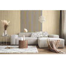 Salon moderne avec des panneaux muraux clairs aspect bois et des lattes noires verticales derrière un canapé d'angle gris.