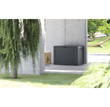 Coffre de jardin moderne en plastique avec structure en bois devant un mur en béton dans un espace extérieur lumineux et organisé.