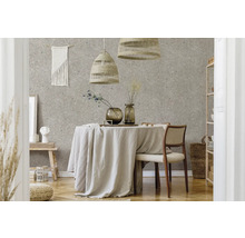 Salle à manger moderne avec papier peint terrazzo, table ronde avec nappe en lin, suspensions tressées et meubles clairs en matières naturelles.