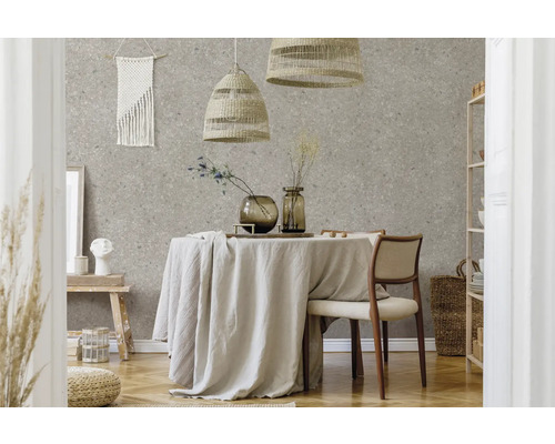 Salle à manger moderne avec papier peint terrazzo, table ronde avec nappe en lin, suspensions tressées et meubles clairs en matières naturelles.