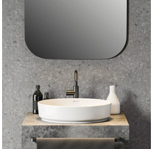 Salle de bains moderne avec vasque à poser ronde blanche, robinetterie noire, mur aspect terrazzo et miroir aux coins arrondis.