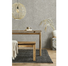 Papier peint intissé aspect pierre en gris, associé à une table en bois, un banc en bois, un tapis tissé foncé et une suspension en osier.