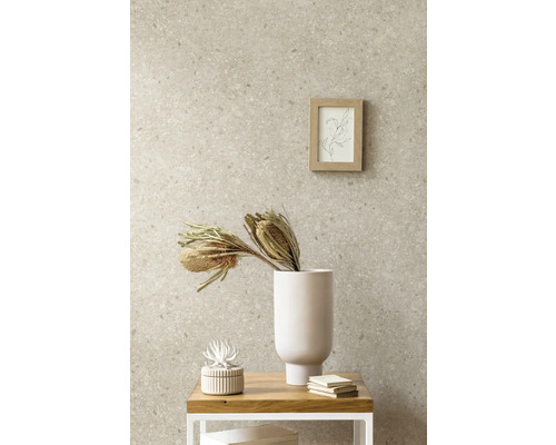 Papier peint intissé aspect pierre avec motif terrazzo dans une pièce à vivre combiné avec un vase blanc, des fleurs séchées et un cadre en bois.