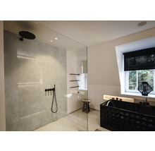 Salle de bain moderne et lumineuse avec douche à l'italienne, robinetterie noire, mur gris effet pierre et baignoire noire texturée.