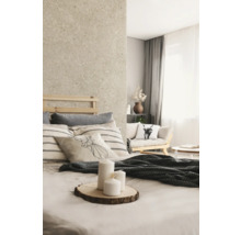 Chambre lumineuse avec mur aspect pierre naturelle, lit en bois, coussins à rayures et bougies blanches sur une tranche de bois.