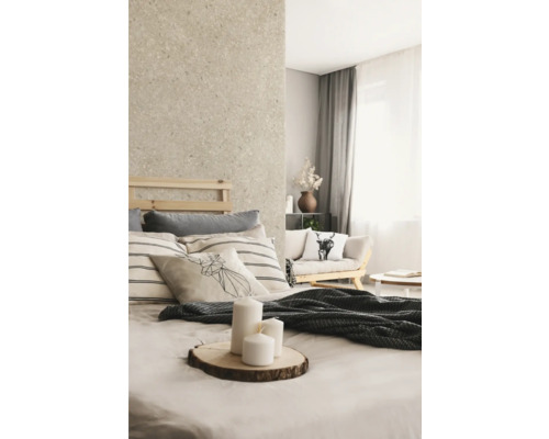 Chambre lumineuse avec mur aspect pierre naturelle, lit en bois, coussins à rayures et bougies blanches sur une tranche de bois.