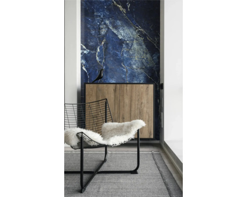 Intérieur avec revêtement mural en marbre bleu, buffet en bois à cadre noir et chaise en fil d'acier avec peau de mouton sur un tapis gris.