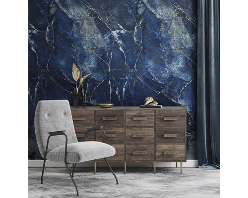 Papier peint panoramique avec motif marbre bleu dans un salon avec commode en bois et fauteuil gris.