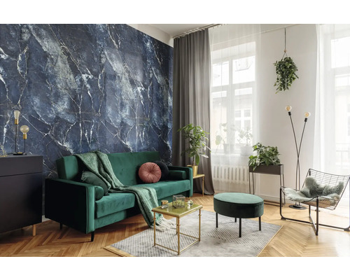 Salon moderne avec papier peint marbre bleu foncé, canapé en velours vert et parquet en chevrons. Décoré avec des plantes et des touches dorées.