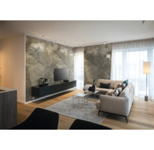 Salon moderne avec mur effet marbre, buffet noir suspendu, canapé d'angle clair, parquet en bois et grandes fenêtres avec rideaux transparents.