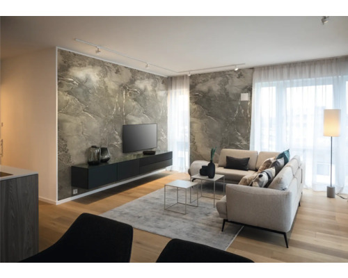 Salon moderne avec mur effet marbre, buffet noir suspendu, canapé d'angle clair, parquet en bois et grandes fenêtres avec rideaux transparents.