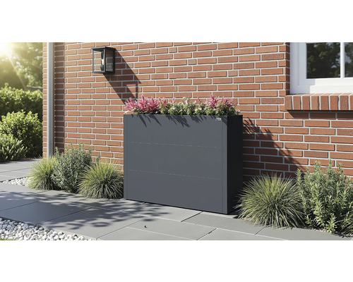 Bac à fleurs en métal anthracite sur une terrasse devant un mur en briques, garni de plantes ornementales.