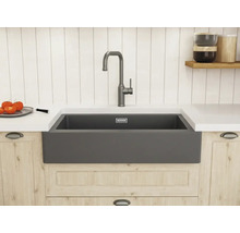 Helle, organisierte Küche im Landhausstil mit anthrazitfarbenem Spülstein, hoher Armatur, Arbeitsplatte und Holzunterschrank vor Paneelwand.