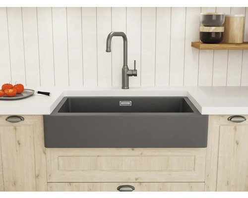 Helle, organisierte Küche im Landhausstil mit anthrazitfarbenem Spülstein, hoher Armatur, Arbeitsplatte und Holzunterschrank vor Paneelwand.