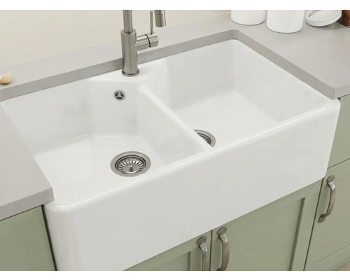 Weiße Doppel-Keramikspüle im Landhausstil mit Armatur aus gebürstetem Metall, eingebaut in eine graue Arbeitsplatte.