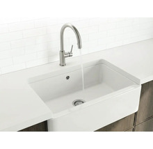 Weißes Spülbecken im Landhausstil mit hohem Wasserhahn aus Metall und fließendem Wasser in einer hellen, organisierten Küche.