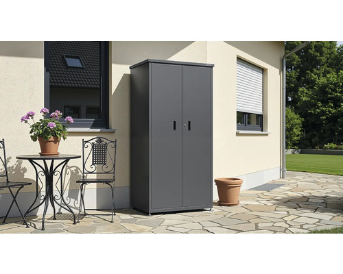 Armoire de jardin en métal gris anthracite avec deux portes sur une terrasse en pierre contre un mur de maison et mobilier de jardin.