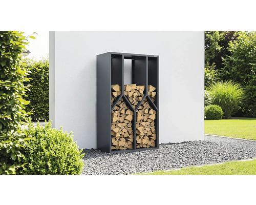 Range-bûches en métal anthracite rempli de bois de chauffage dans un jardin sur du gravier devant un mur.