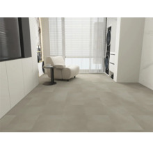 Carrelage de sol grand format gris clair, salon moderne avec fauteuil blanc, table d'appoint et fenêtre, pièce lumineuse et spacieuse.