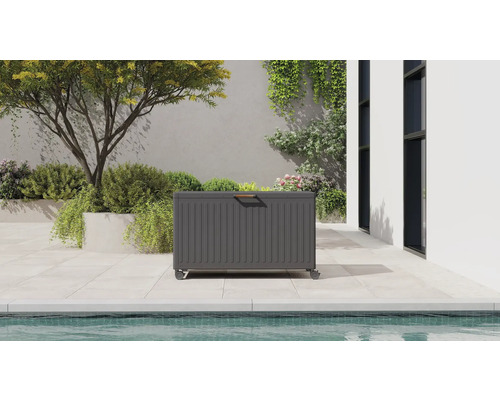 Coffre de jardin gris avec roulettes et poignée en bois sur une terrasse moderne avec piscine et plantes.