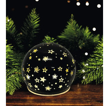 Boule décorative noire avec motif d étoiles dorées devant des branches de sapin sur une surface en bois.
