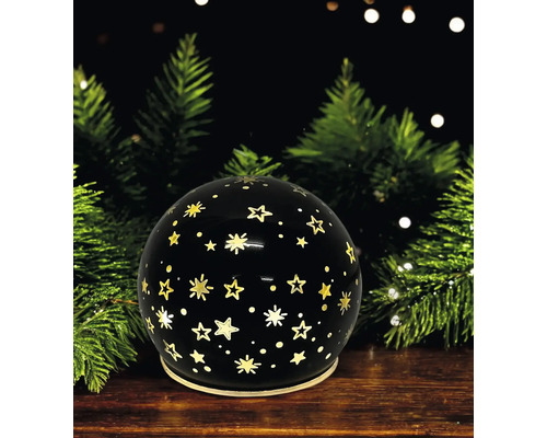 Boule décorative noire avec motif d étoiles dorées devant des branches de sapin sur une surface en bois.