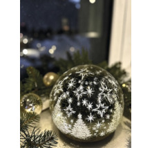 Boule LED en verre avec motif d'étoiles et de sapins de Noël sur des branches de pin.