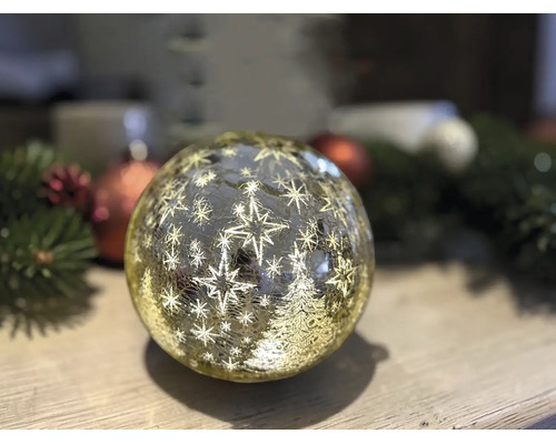 Boule de Noël lumineuse à LED en verre avec motif d'étoiles et de sapin sur une surface en bois.
