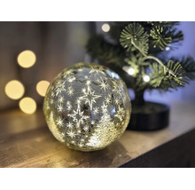 Boule en verre LED illuminée avec motifs d'étoiles et de sapin de Noël en aspect craquelé sur surface en bois à côté d'un petit sapin de Noël.
