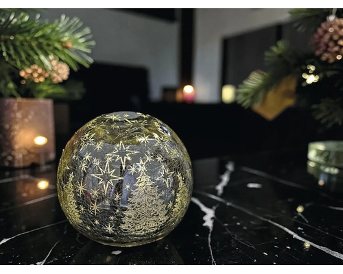 Boule lumineuse en verre LED avec étoiles et sapins sur une table en marbre sombre dans une ambiance de Noël.