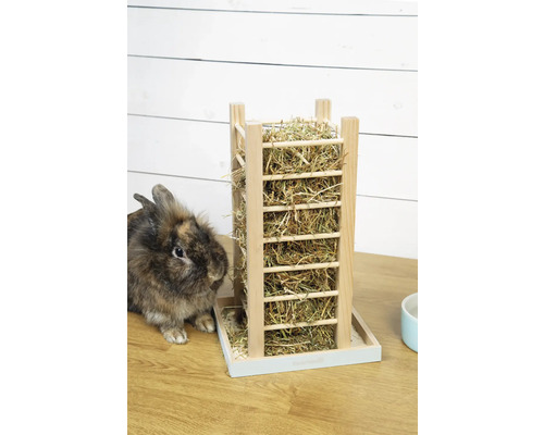 Heuraufe aus Holz für Kaninchen mit Auffangschale, gefüllt mit Heu, auf einem Holztisch neben einem Kaninchen.