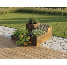Jardinière surélevée modulaire en acier Corten dans un jardin avec des plantes, à côté d'une terrasse en bois et d'un chemin en pierre.