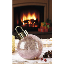 Boule de Noël à LED en verre craquelé avec attache dorée devant une cheminée allumée avec des pommes de pin et des cadeaux.